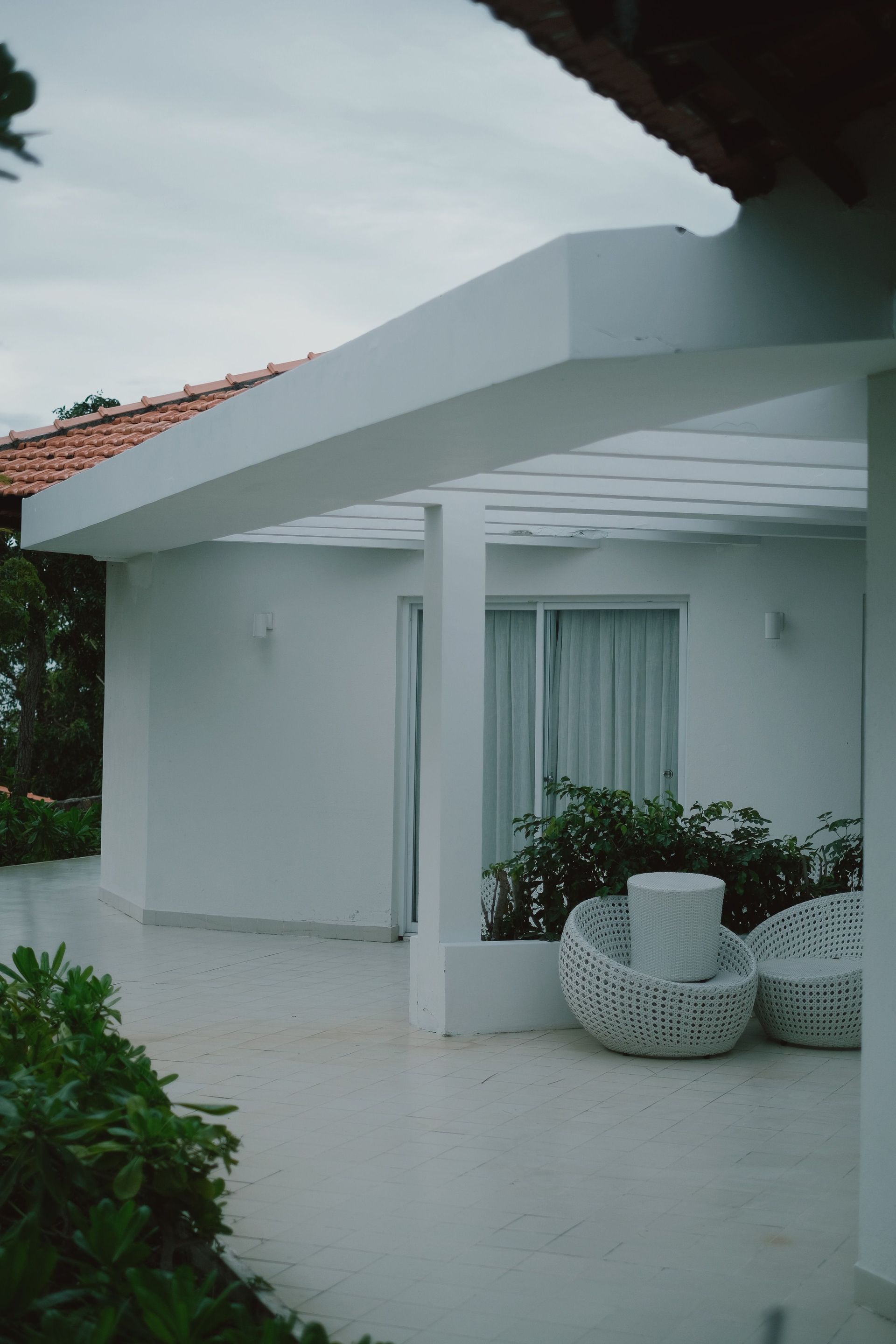 Minimalist patio space with white furniture and greenery creates a serene outdoor setting.